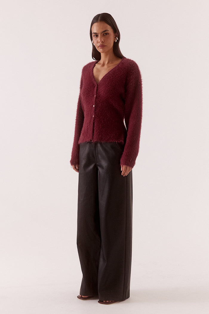 Woman wearing a burgundy cardigan and dark pants on a white background