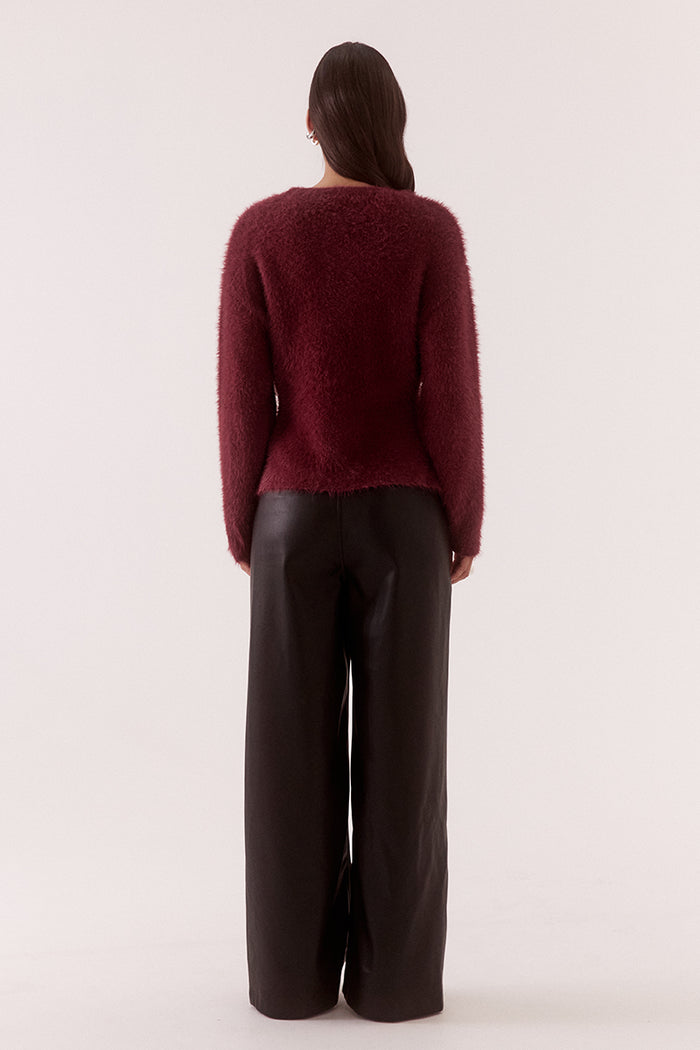 Person wearing a burgundy sweater and black pants on a white background