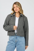 Woman wearing a gray jacket over a white shirt and blue jeans on a light gray background