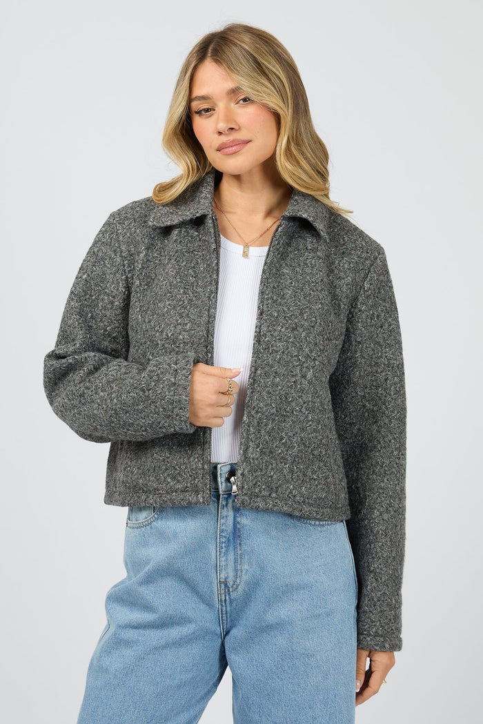 Woman wearing a gray jacket over a white shirt and blue jeans on a light gray background