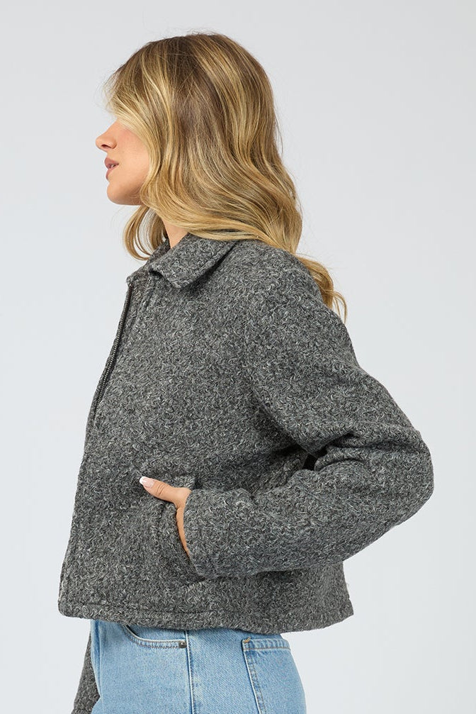 Person wearing a gray jacket and light blue jeans on a white background
