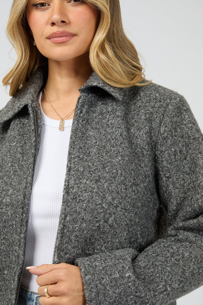 Woman wearing a gray coat over a white shirt on a plain background