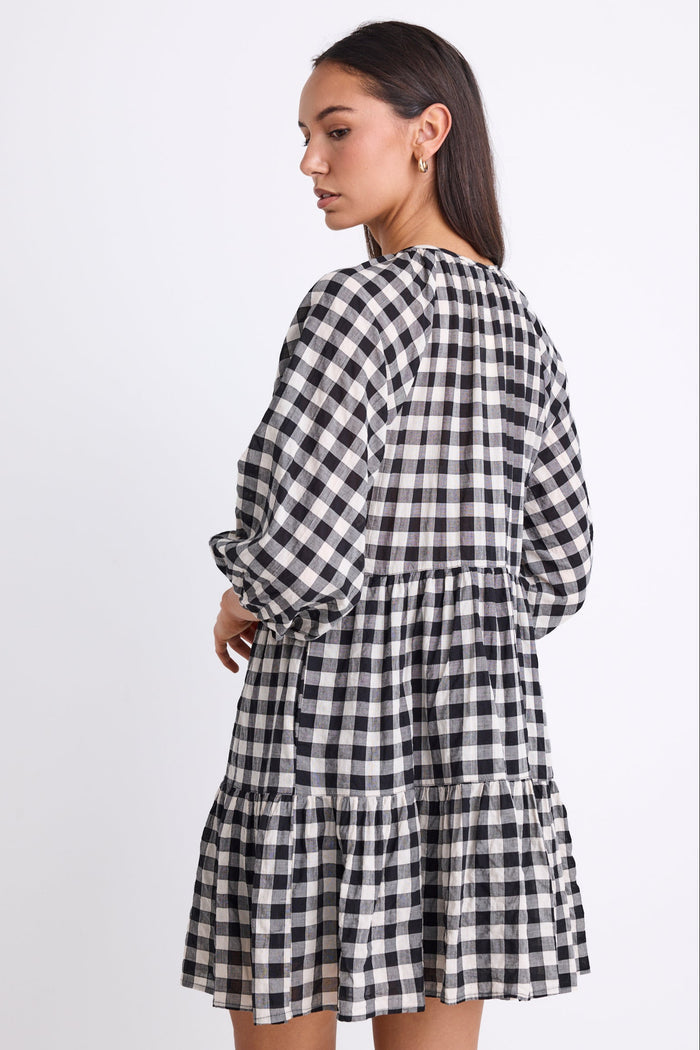 Woman wearing a black and white gingham mini dress with a button-down front, tiered skirt, and mid-length sleeves.