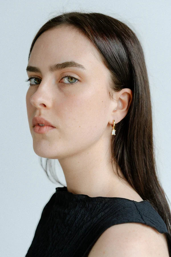 Woman with long brown hair wearing a black top against a light background