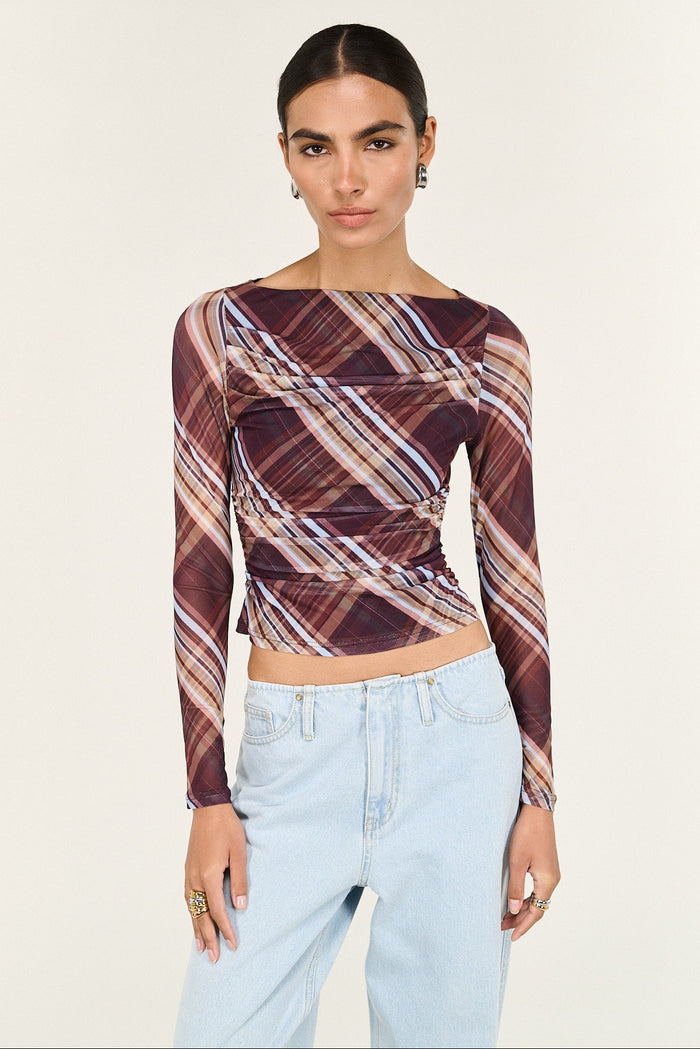 Woman wearing a patterned long-sleeve top and light blue jeans on a white background