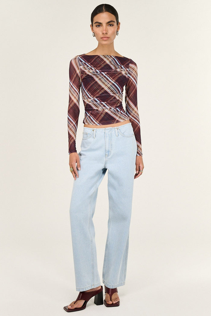 Woman wearing a patterned top and light blue jeans on a white background