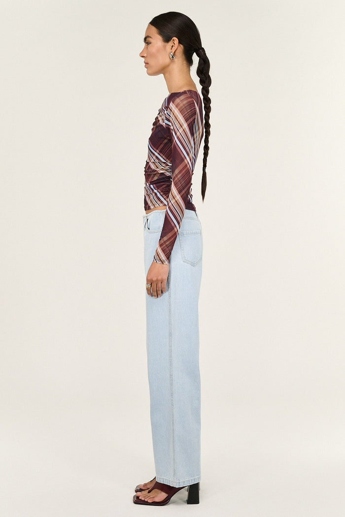 Woman wearing a patterned top and light blue jeans on a white background