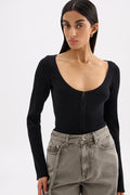 A woman wearing a black ribbed long-sleeve scoop-neck top with a front zipper, paired with gray high-waisted jeans, against a plain light gray background.