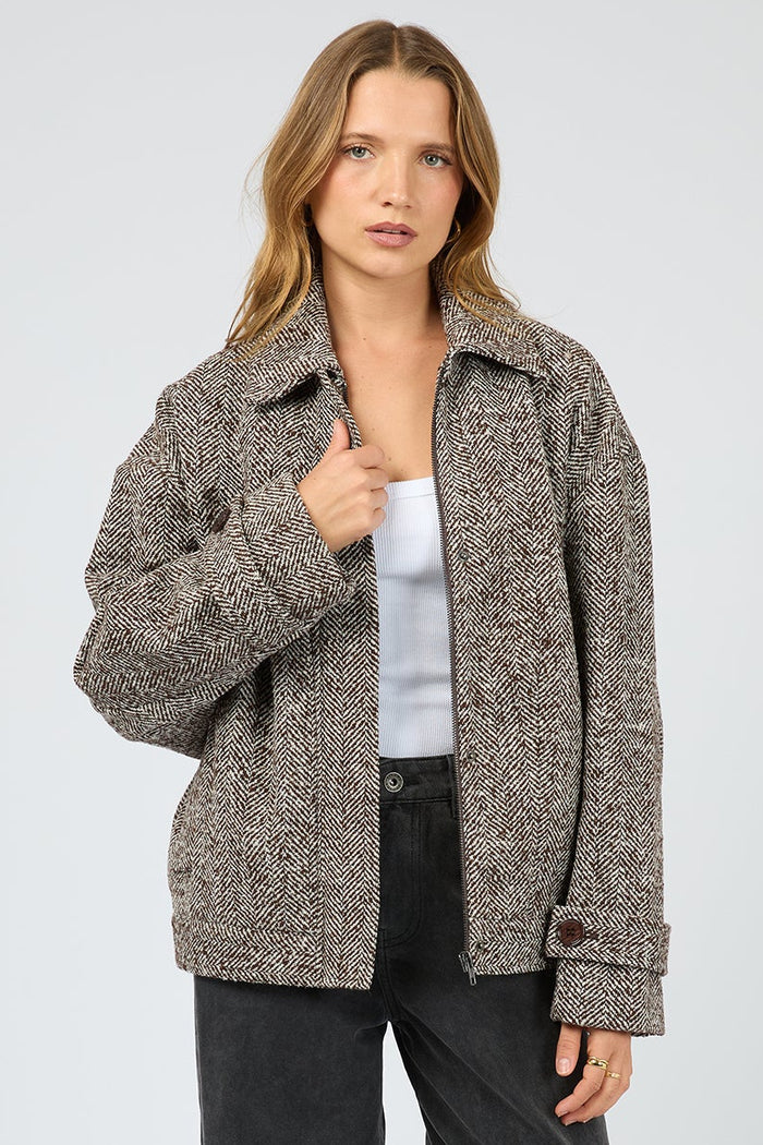 Woman wearing a brown textured jacket and black pants on a white background