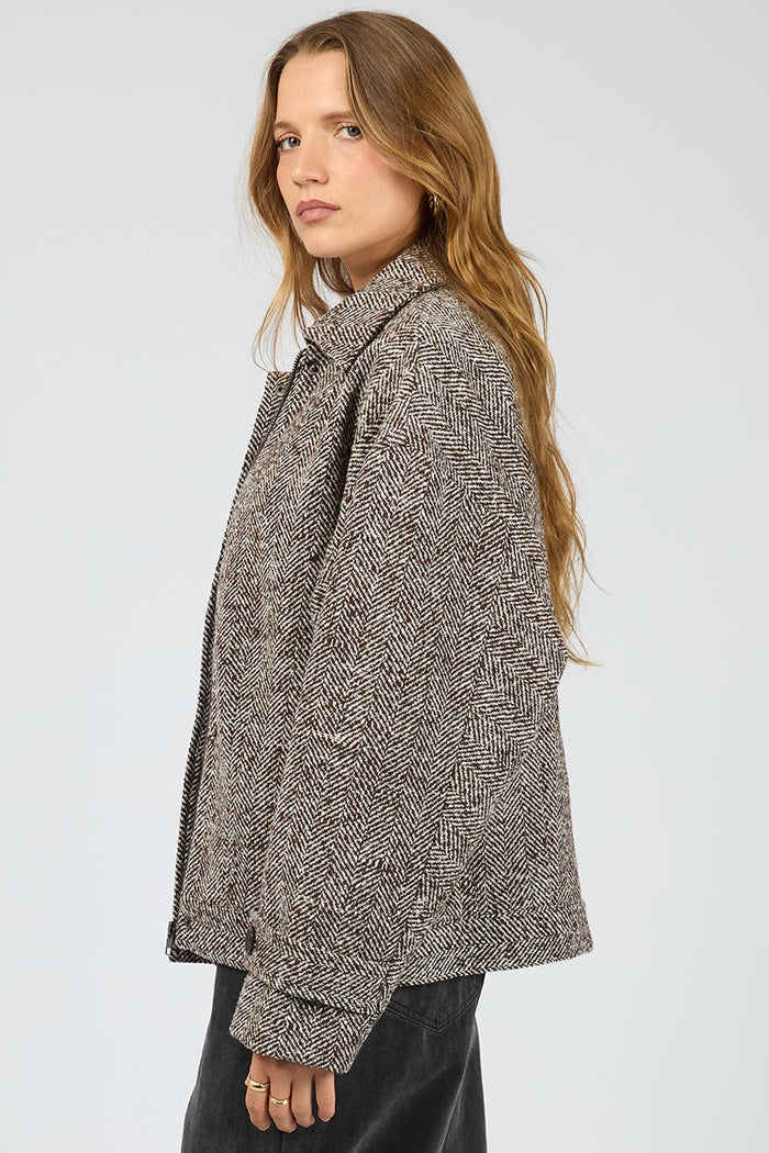 Person wearing a textured brown jacket and black pants on a white background