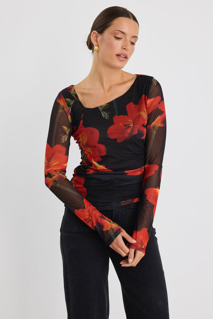 Woman wearing a fitted long sleeve mesh top with bold red floral print and sheer sleeves, paired with black jeans.