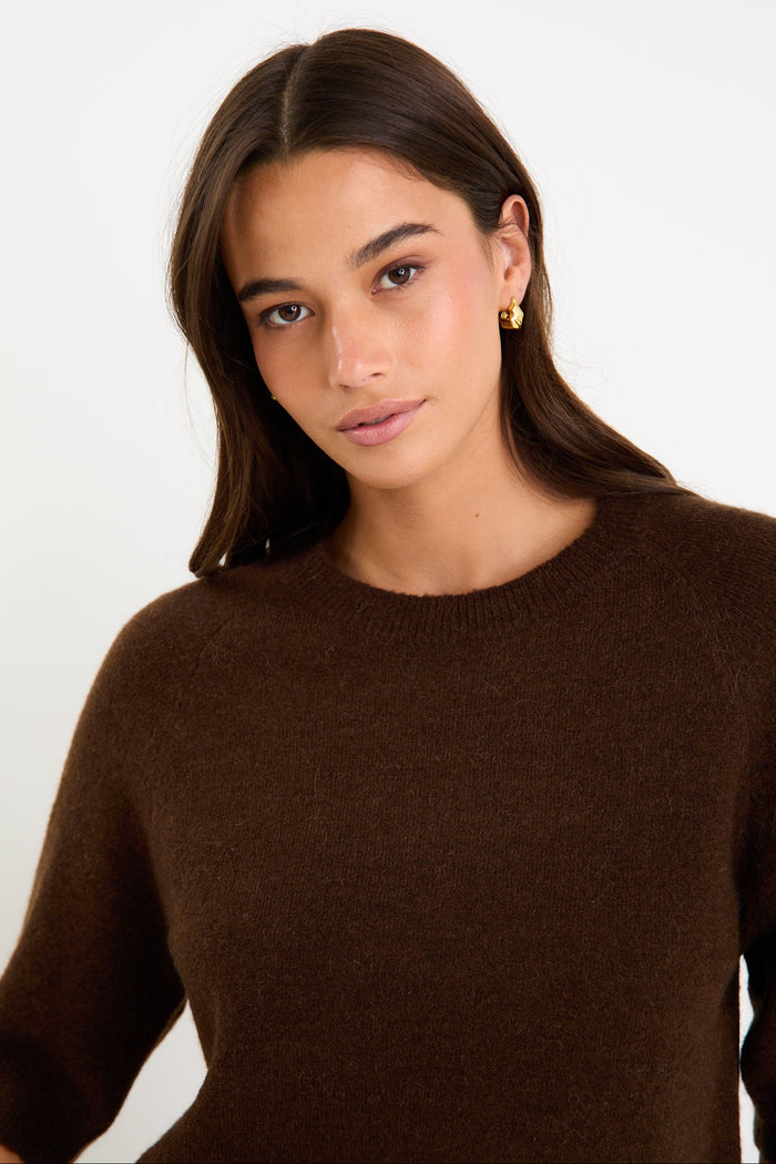 Woman wears a chocolate knit tee and blue jeans with brown loafers