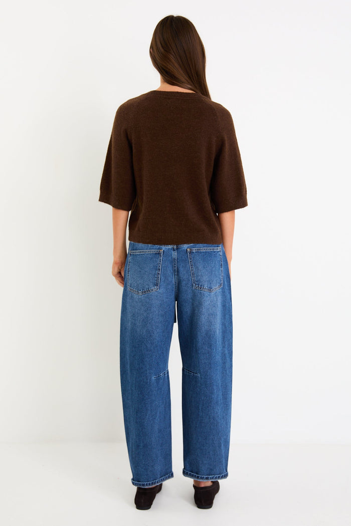 Woman wears a chocolate knit tee and blue jeans with brown loafers