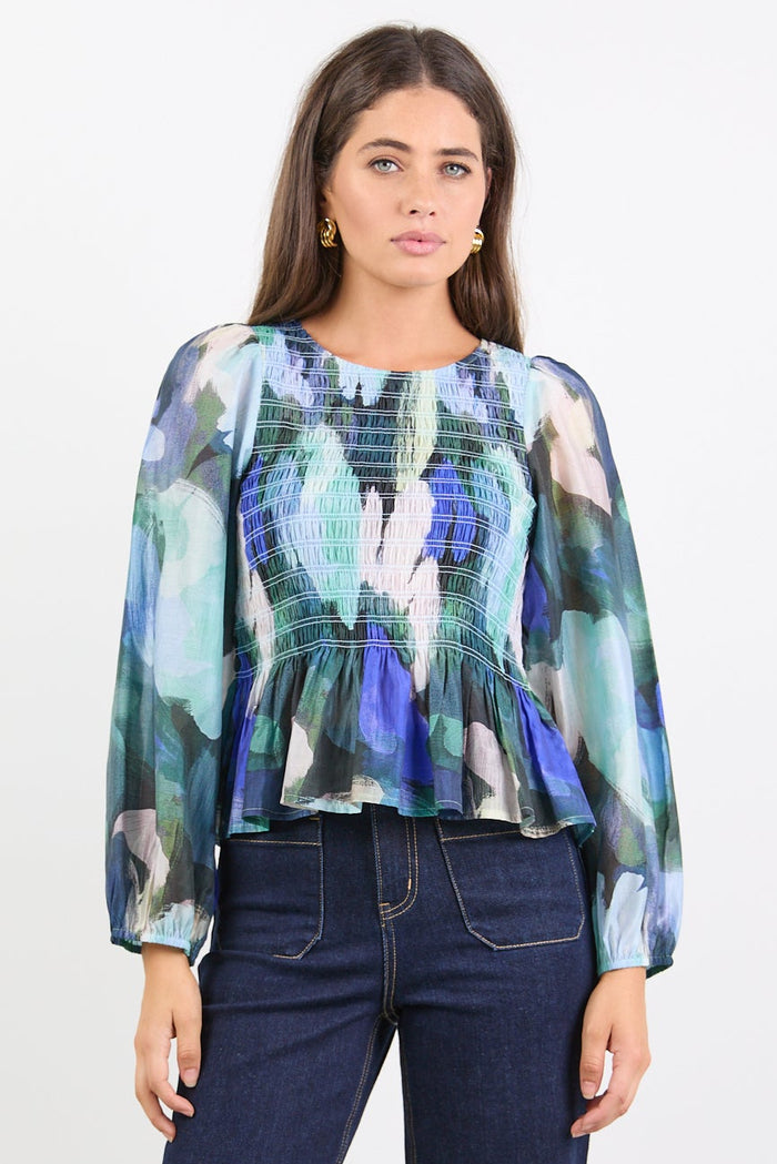 Woman wearing a colorful blouse and dark jeans on a white background