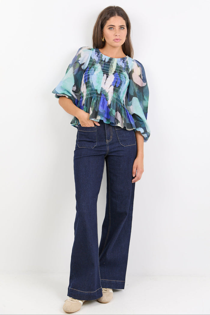 Woman wearing a colorful blouse and dark blue jeans against a white background