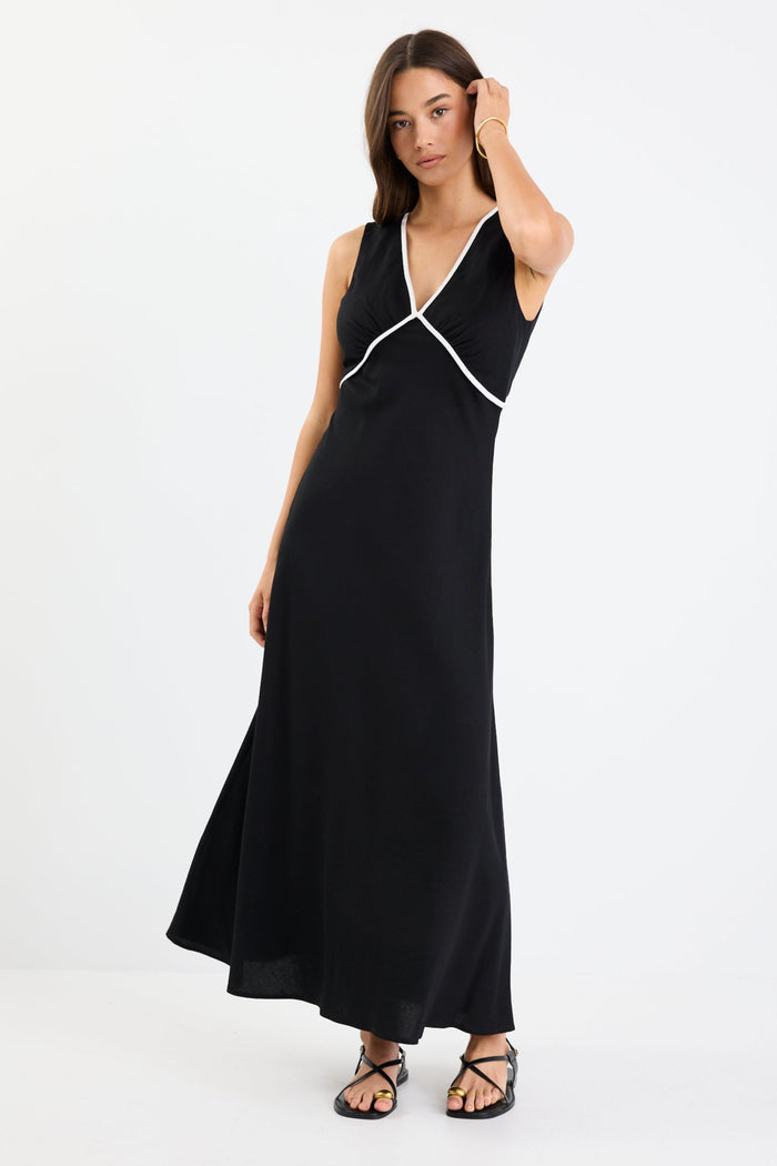 Woman wearing a black sleeveless maxi dress with a V-neckline, white contrast binding detail, bias cut, and softly flared hem.