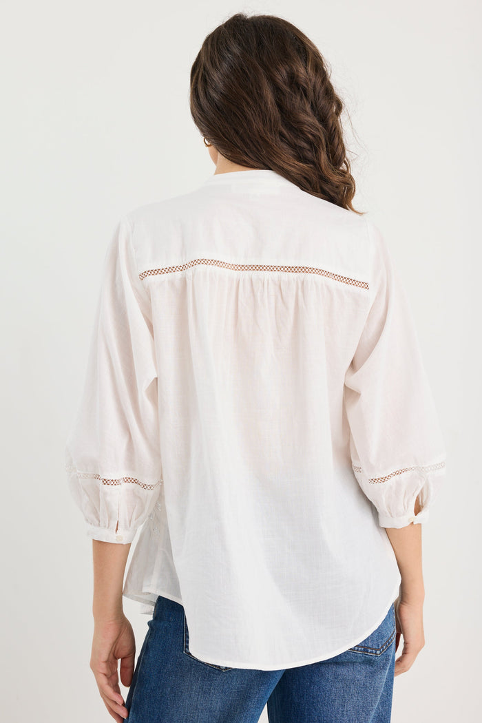 Woman wearing a white blouse with lace details and blue jeans on a white background