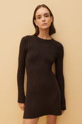 Woman wearing a black ribbed dress against a beige background
