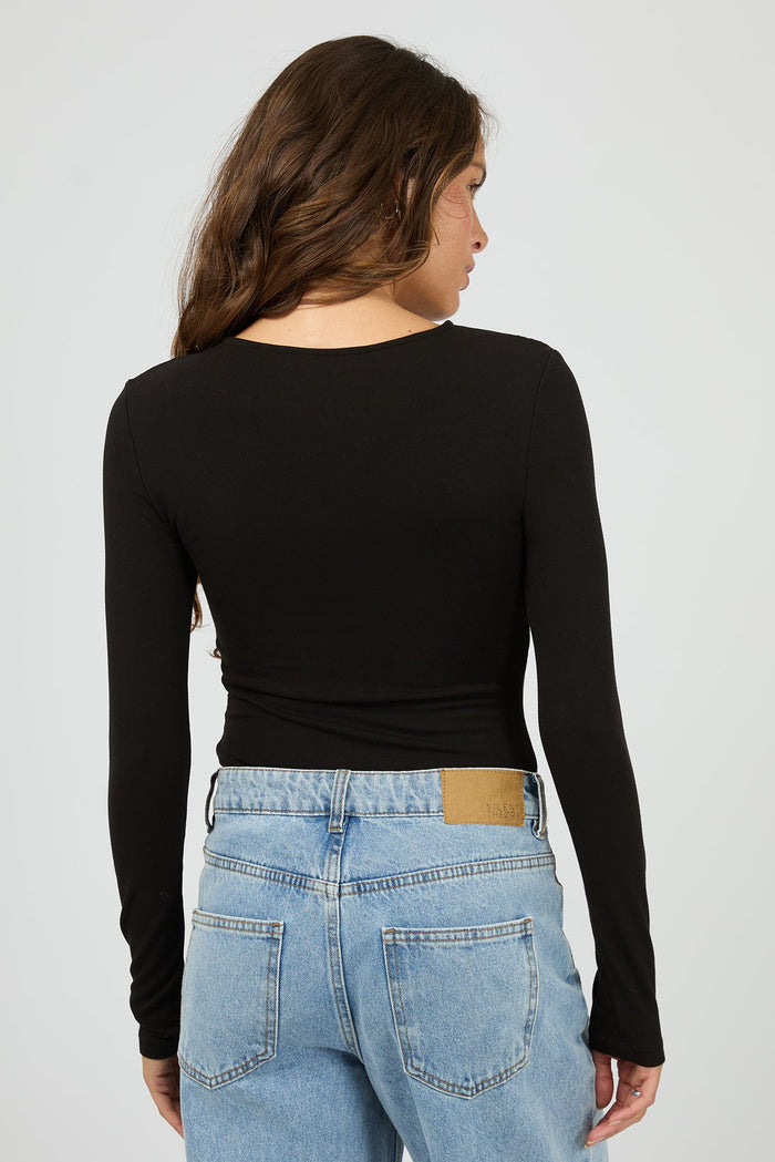 Person wearing a black long-sleeve top and light blue jeans on a plain background
