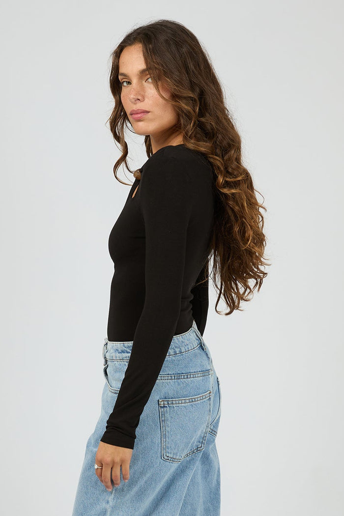 Woman wearing light blue jeans and a black top on a white background