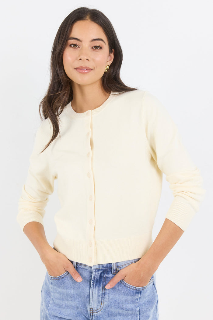 Woman wearing a light-colored cardigan and blue jeans against a white background