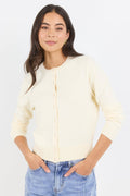 Woman wearing a light-colored cardigan and blue jeans against a white background