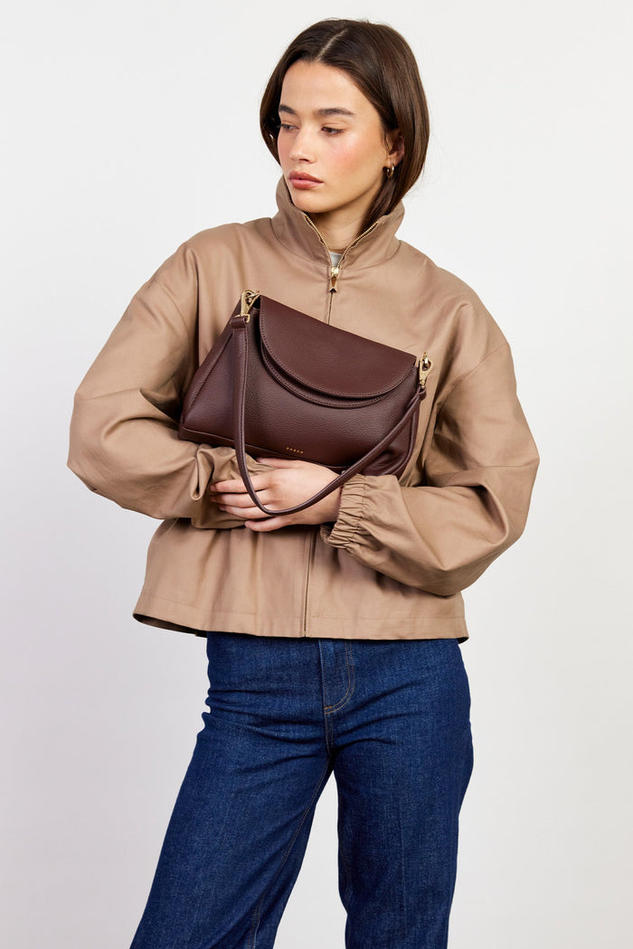 Woman holding a brown leather handbag against a plain background