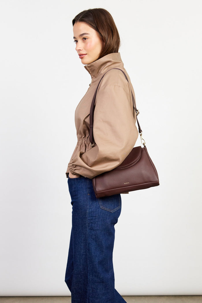 Woman holding a brown handbag against a white background