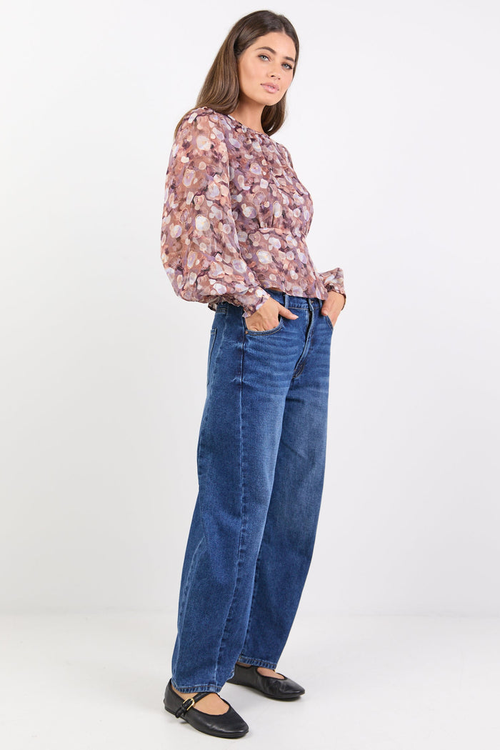 Woman wearing a patterned blouse and blue jeans on a white background