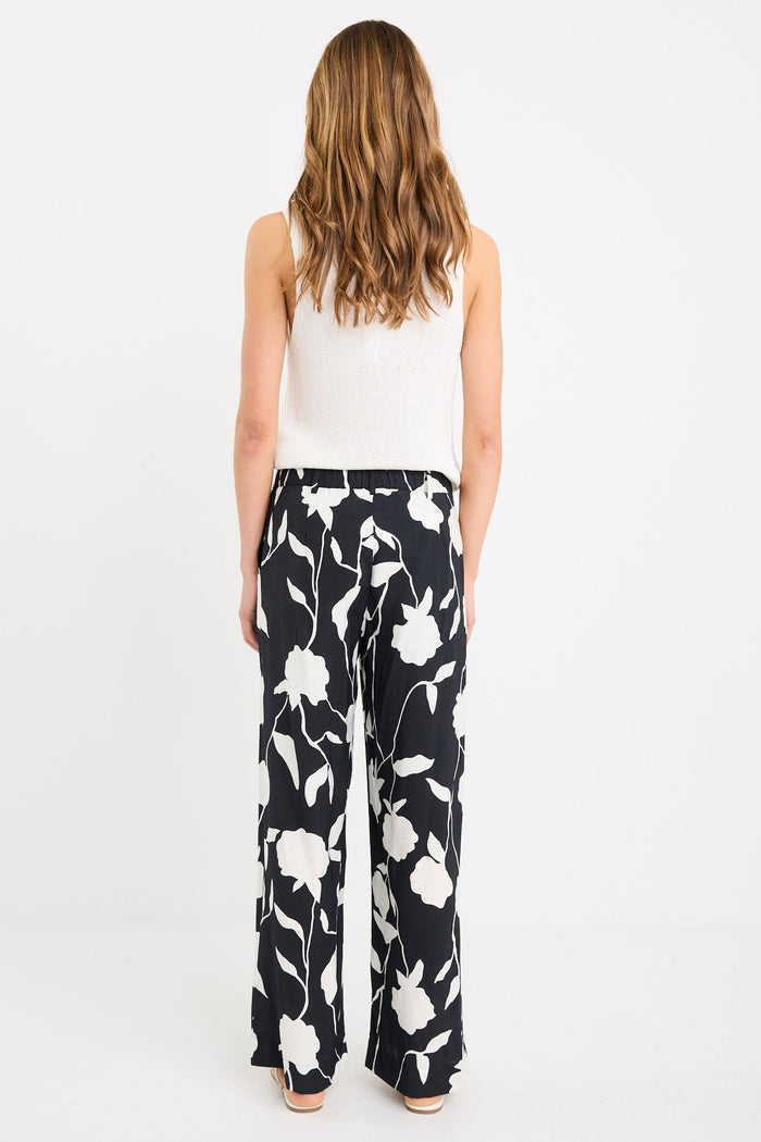 Woman wearing a white sleeveless top and black floral pants on a white background