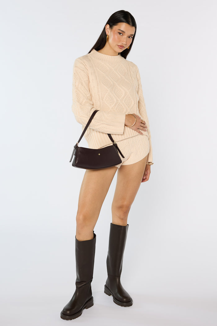 Woman wearing a beige sweater, shorts, and black knee-high boots on a white background