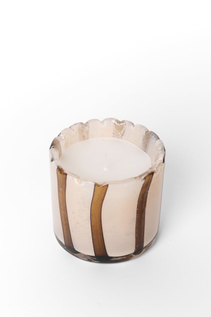 A small candle in a scalloped glass holder with vertical brown and beige stripes, photographed on a clean white background.