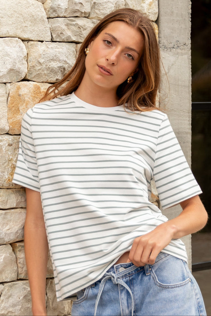 Woman wearing a striped shirt and jeans standing against a stone wall.