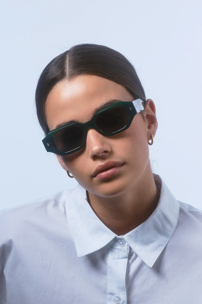 Person wearing dark sunglasses and a light-colored shirt against a plain background