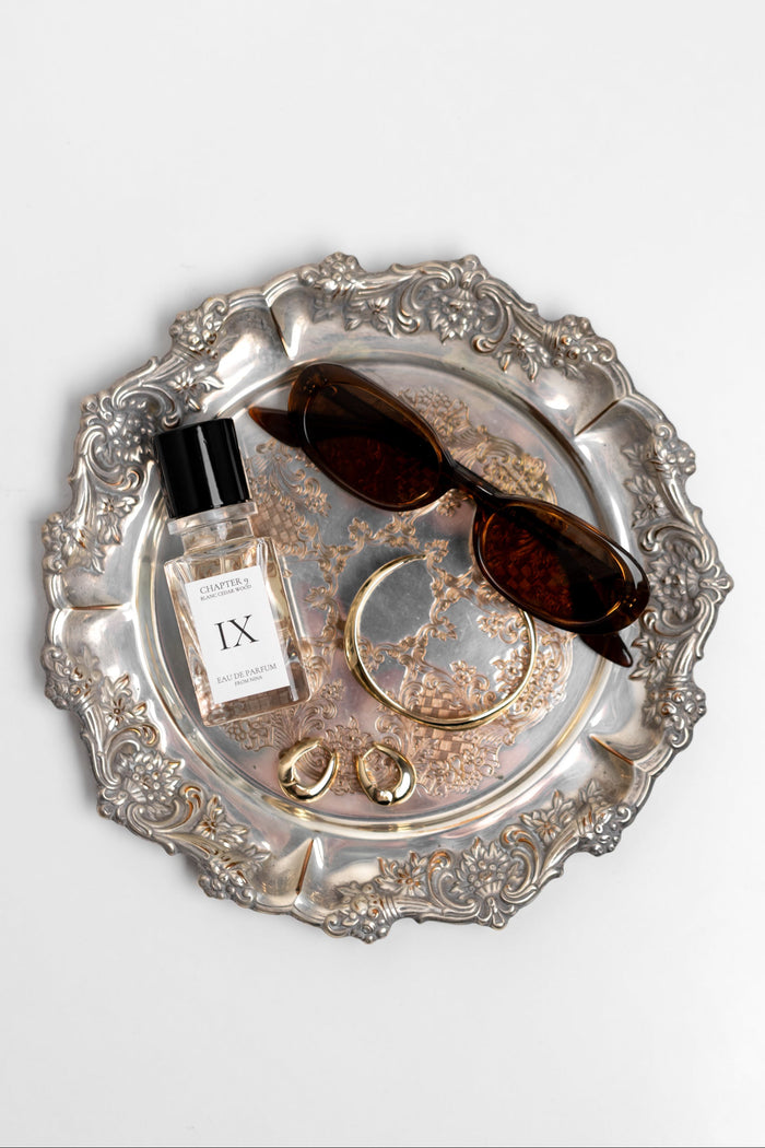Silver tray with a bottle of perfume, sunglasses, and jewelry on a white background