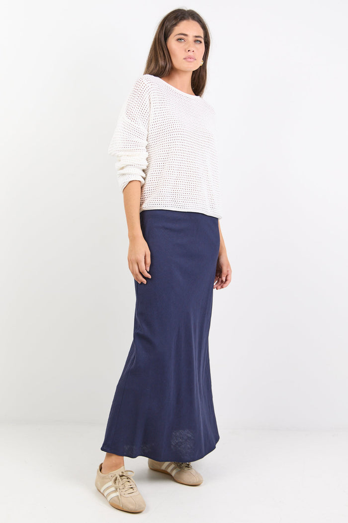 Woman wearing a white sweater and navy skirt on a white background
