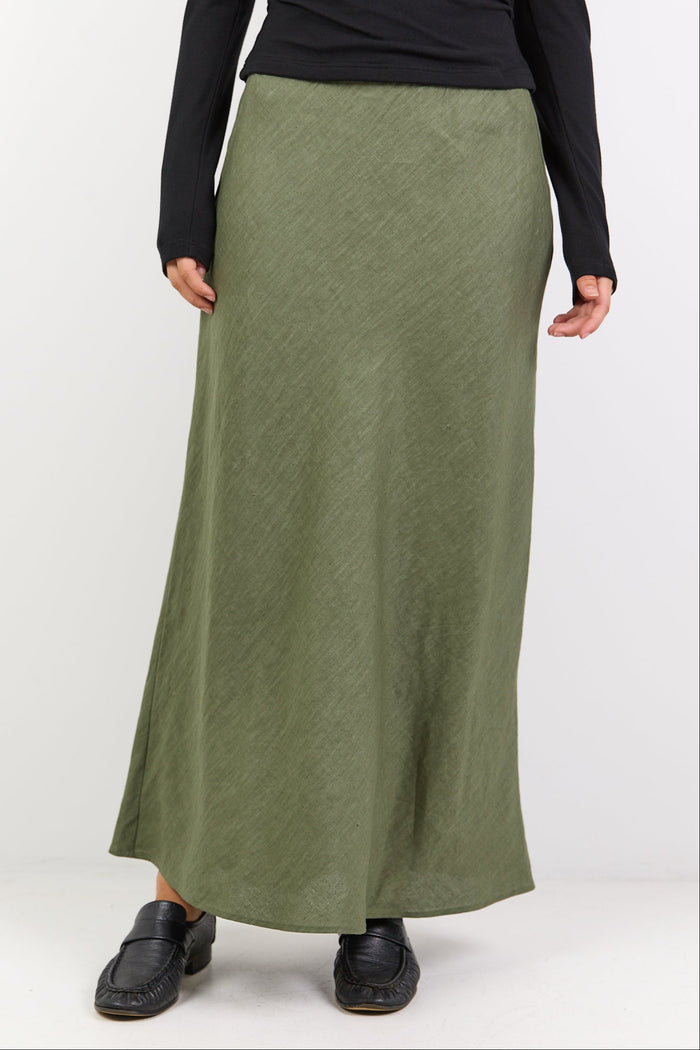 Person wearing a black long-sleeve top and green skirt on a white background