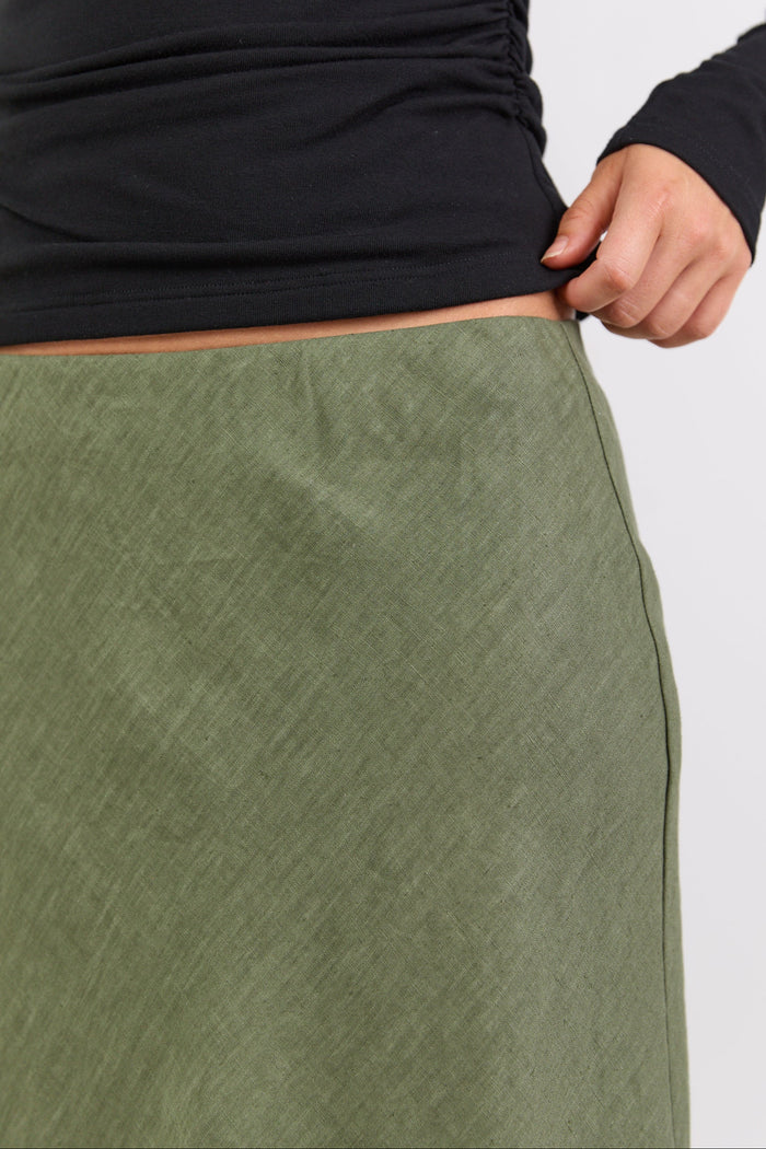 Person wearing a black long-sleeve top and green pants on a light gray background