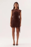 A woman modeling a brown sheer mesh mini dress with a dark brown polka dot pattern, photographed against a seamless white studio background.