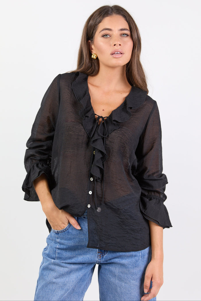 Woman wearing a black blouse with ruffled details and blue jeans on a white background