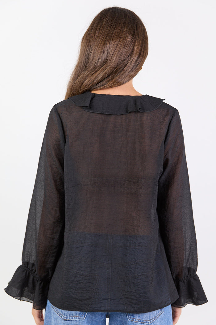 Person wearing a black sheer blouse with long sleeves and ruffled cuffs on a white background