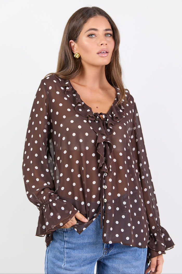 Woman wearing a brown polka dot blouse with blue jeans on a white background