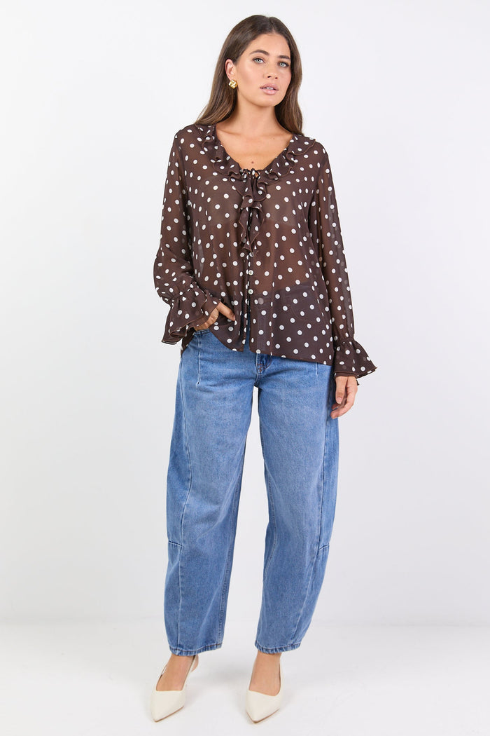 Woman wearing a brown polka dot blouse and blue jeans on a white background