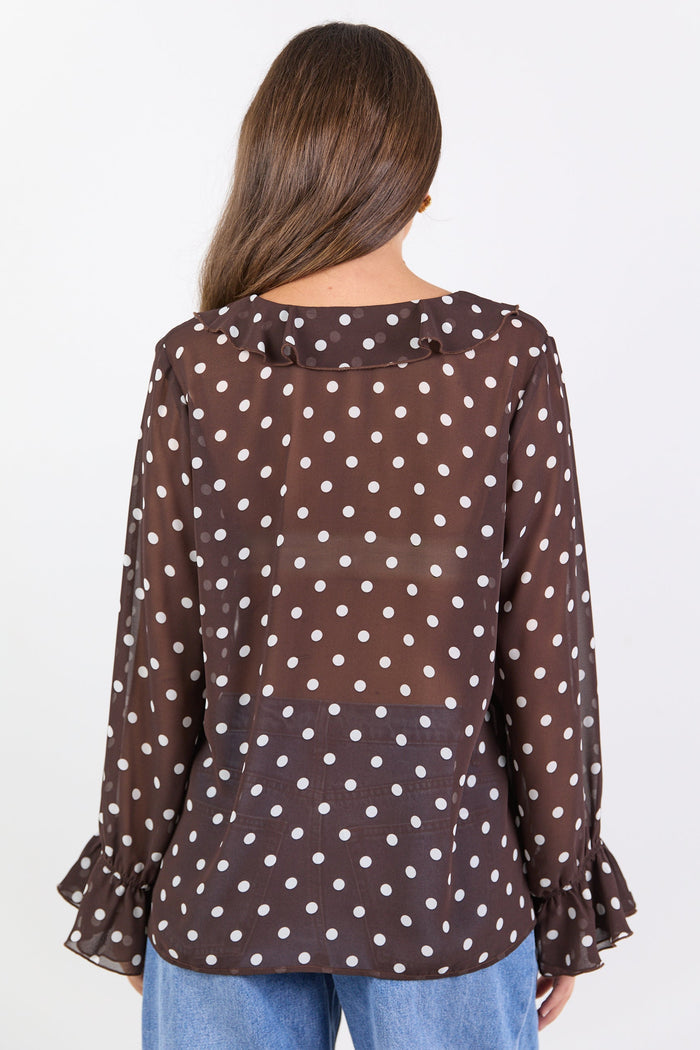 Woman wearing a brown polka dot blouse with blue jeans on a white background