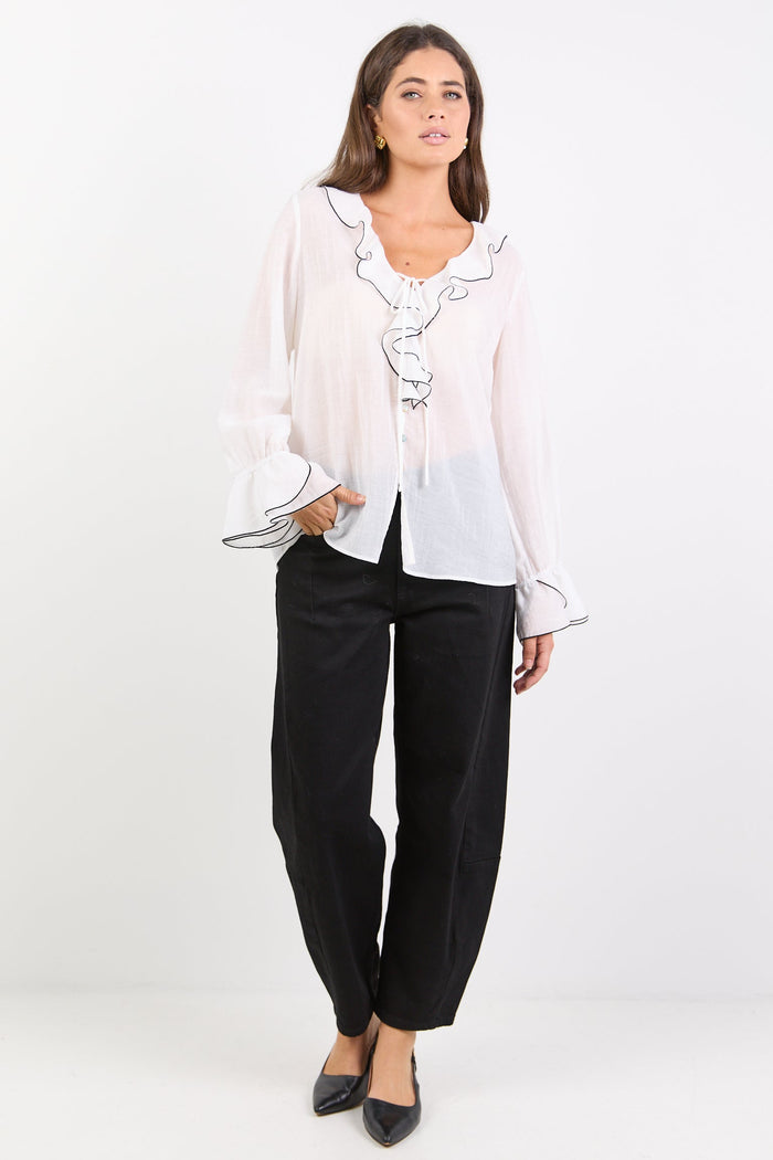 Woman wearing a white blouse with ruffled details and black pants on a white background