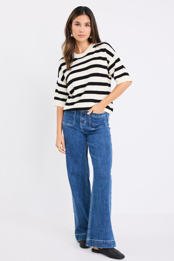 Woman wearing a short-sleeved black and ivory striped cotton tee with a crew neckline, styled casually with denim jeans.