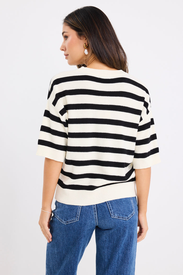 Woman wearing a short-sleeved black and ivory striped cotton tee with a crew neckline, styled casually with denim jeans.