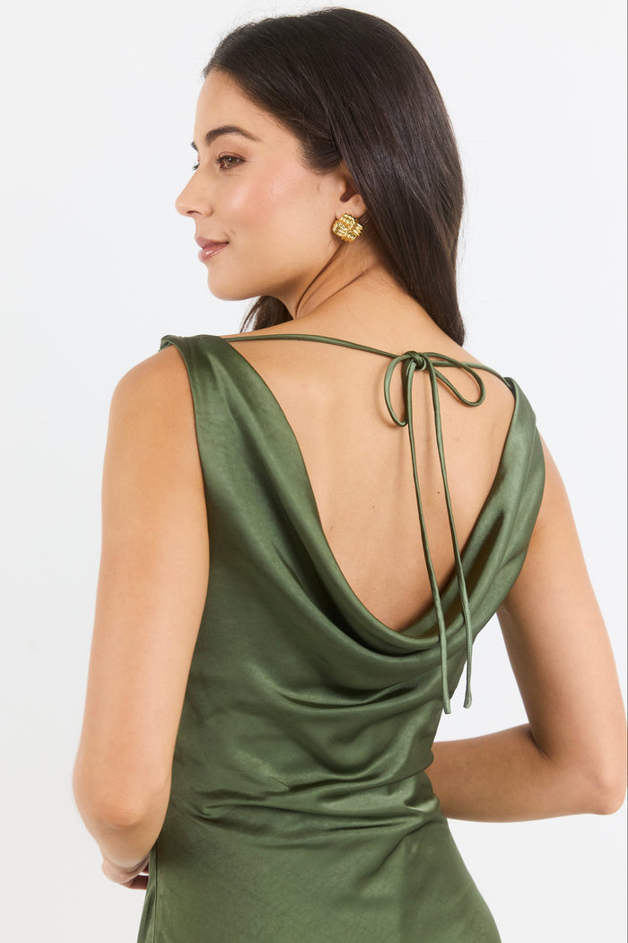 A woman shown from the back wearing an olive green satin slip dress with a tie-back neckline, photographed against a clean white studio background.