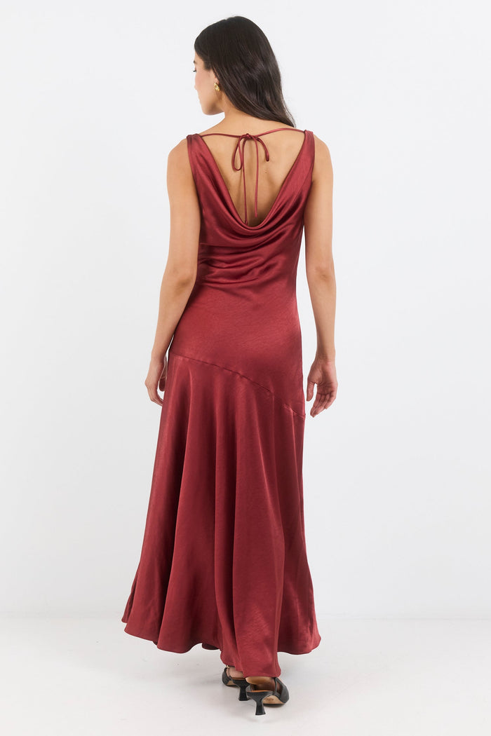 Woman wearing a burgundy dress with a draped back design on a white background
