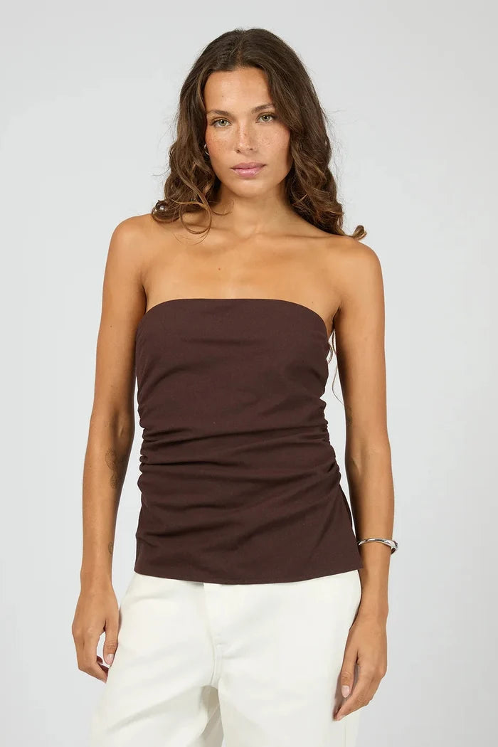 Woman wearing a brown strapless top and white pants on a plain background